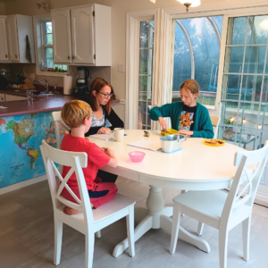 mom and two kids sitting at table reading during morning homeschool routine